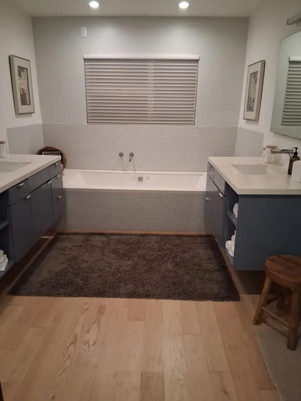 Primary bathroom with two blue vanities and a tiled soaking tub, towels rolled on the open shelves, after a regular cleaning in Beverly Hills